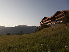Das Hotel Le Grand Chalet auf einem Hügel, blauer Himmel, ein Feld mit Bäumen und ein Berg im Hintergrund.
