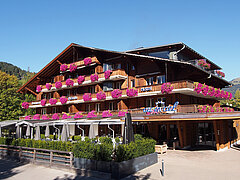 View of the Hotel Arc-en-Ciel decorated with flowers. The terrace can be seen in the foreground behind green plants.
