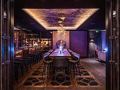 An illuminated room with a table in the center and a bar on the left side