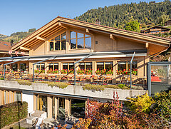 Das Hotel von der Frontansicht mit Terasse und Blumengarten am rechten Bildrand