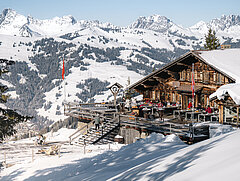 A mountain restaurant with a terrace and lots of snow, in front of mountains beautifully blanketed with snow.