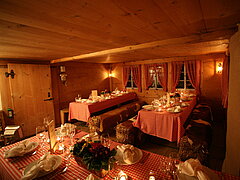 Salle au décor rustique dans laquelle se trouvent des tables couvertes de nappes à carreaux rouges et blancs, dressées pour le dîner. Bancs en bottes de paille recouvertes de peaux de vache.