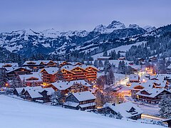Un paysage d'hiver pittoresque avec des collines enneigées et un charmant village. Les maisons sont illuminées et entourées de montagnes majestueuses.