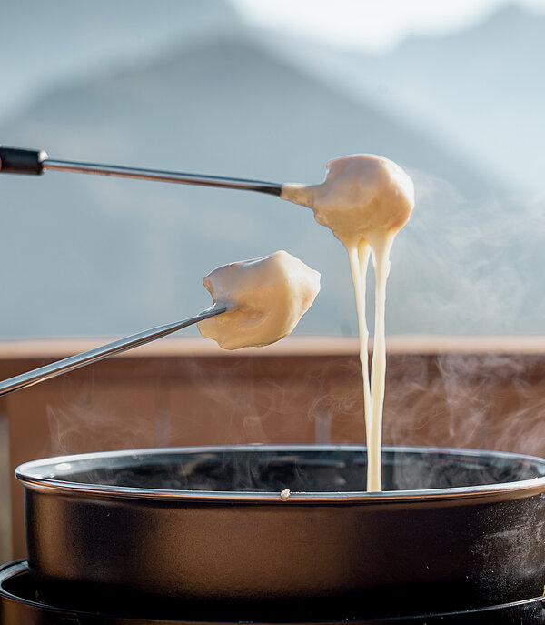 Gros plan sur un caquelon à fondue et deux mains qui trempent du pain dans le fromage avec la fourchette à fondue.