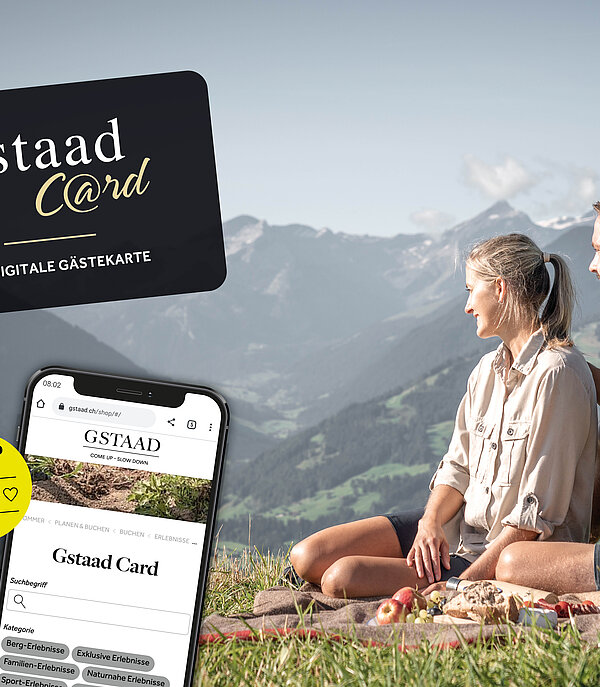 Rechts ein Mann und eine Frau, welche auf einer Picknick-Decke sitzen auf einem Berg und die Aussicht geniessen und links ein Werbebanner für die Gstaad Card.