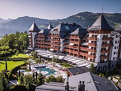 Ein luxuriöses Hotel mit einem schönen Swimmingpool und gepflegten Gärten. Im Hintergrund erheben sich majestätische Berge unter einem klaren Himmel.