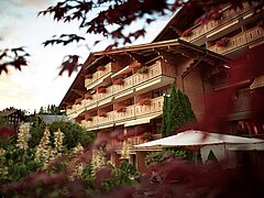 Das Hotel Gstaaderhof mit Balkonen und Blumen. Im Vordergrund steht eine Gruppe von Bäumen.
