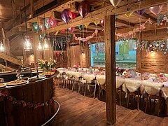 Ein Raum mit Altholz, in der Mitte ein dekorierter Tisch und links eine kleine Bar