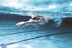 A swimmer with swimming cap and goggles diving in an indoor pool.