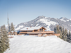 The wooden mountain restaurant in focus on the snow-covered local mountain Eggli. 