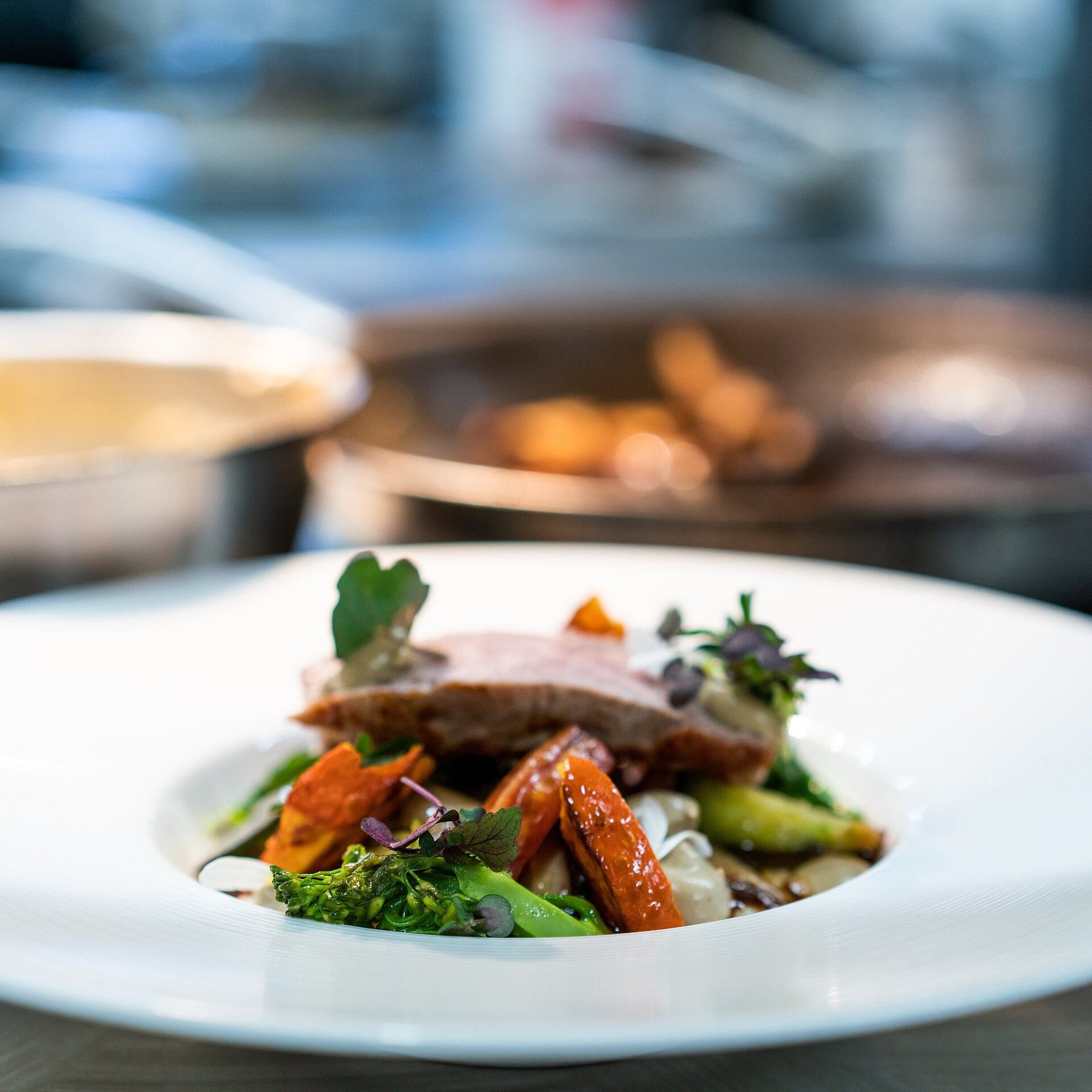 Assiette blanche remplie de viande et de légumes, avec des poêles en arrière-plan.
