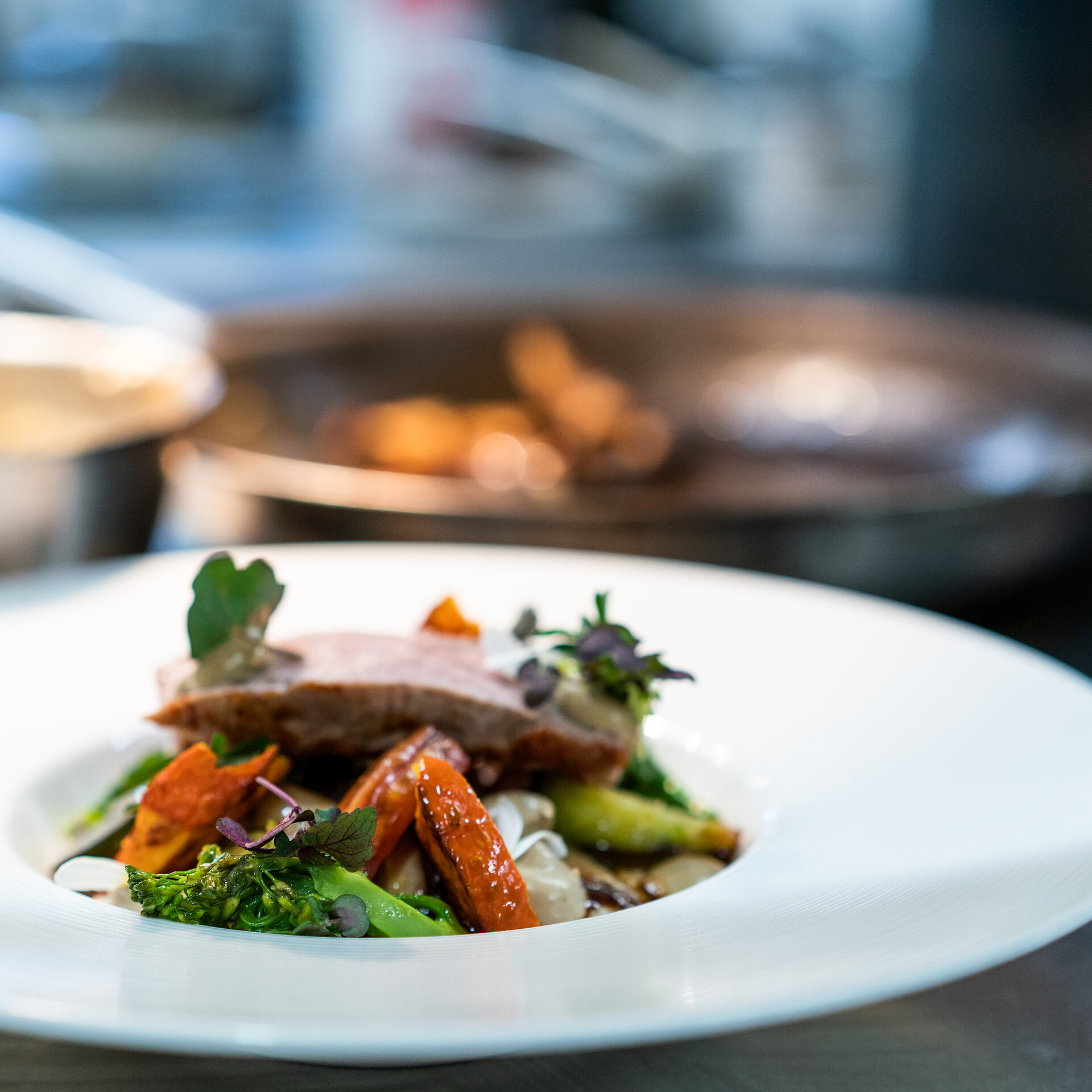 A white plate laden with meat and vegetables, and pans in the background.